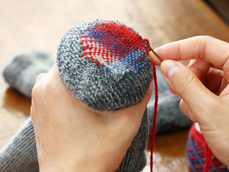 A person is hand stitching using darning supplies.